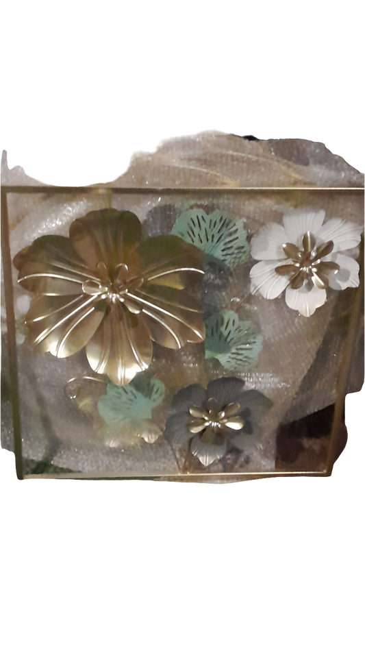 A square metal wall art piece featuring three-dimensional metal flowers and leaves in a gold frame